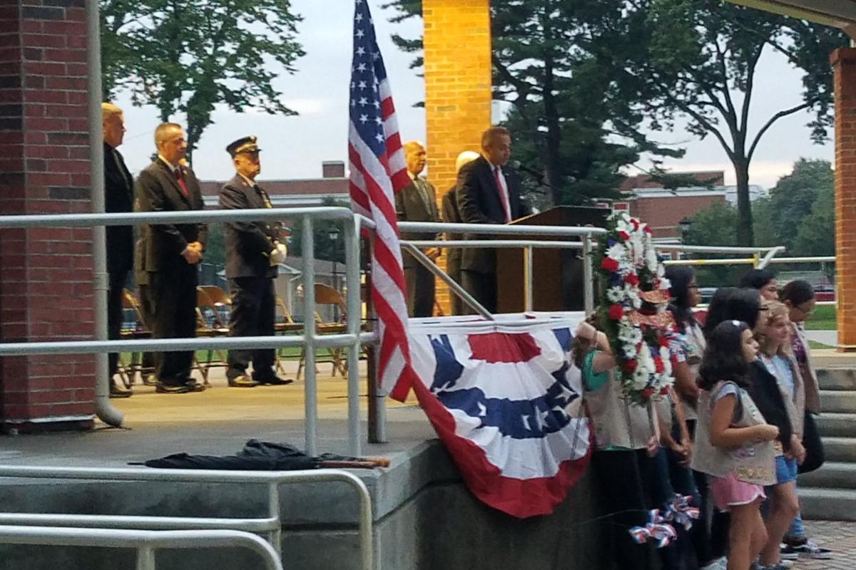 Men on stage on left, American flag and bunting in center, girl scouts in front of stage on right