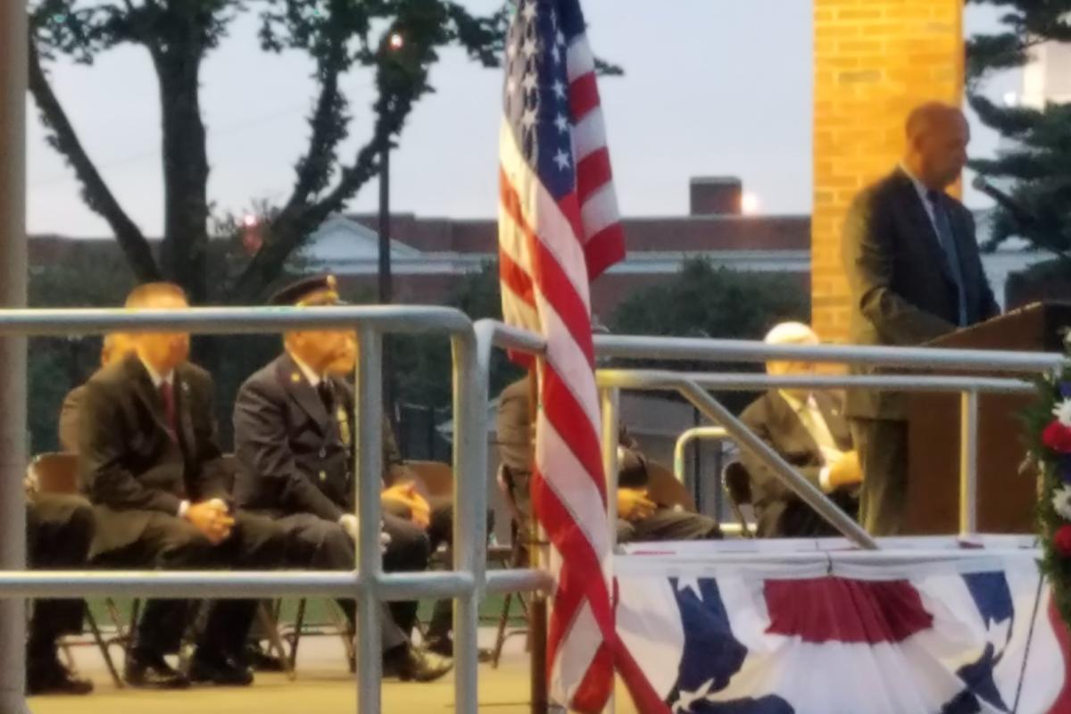 Men seated on left, American flag in center, Mayor standing at podium on right