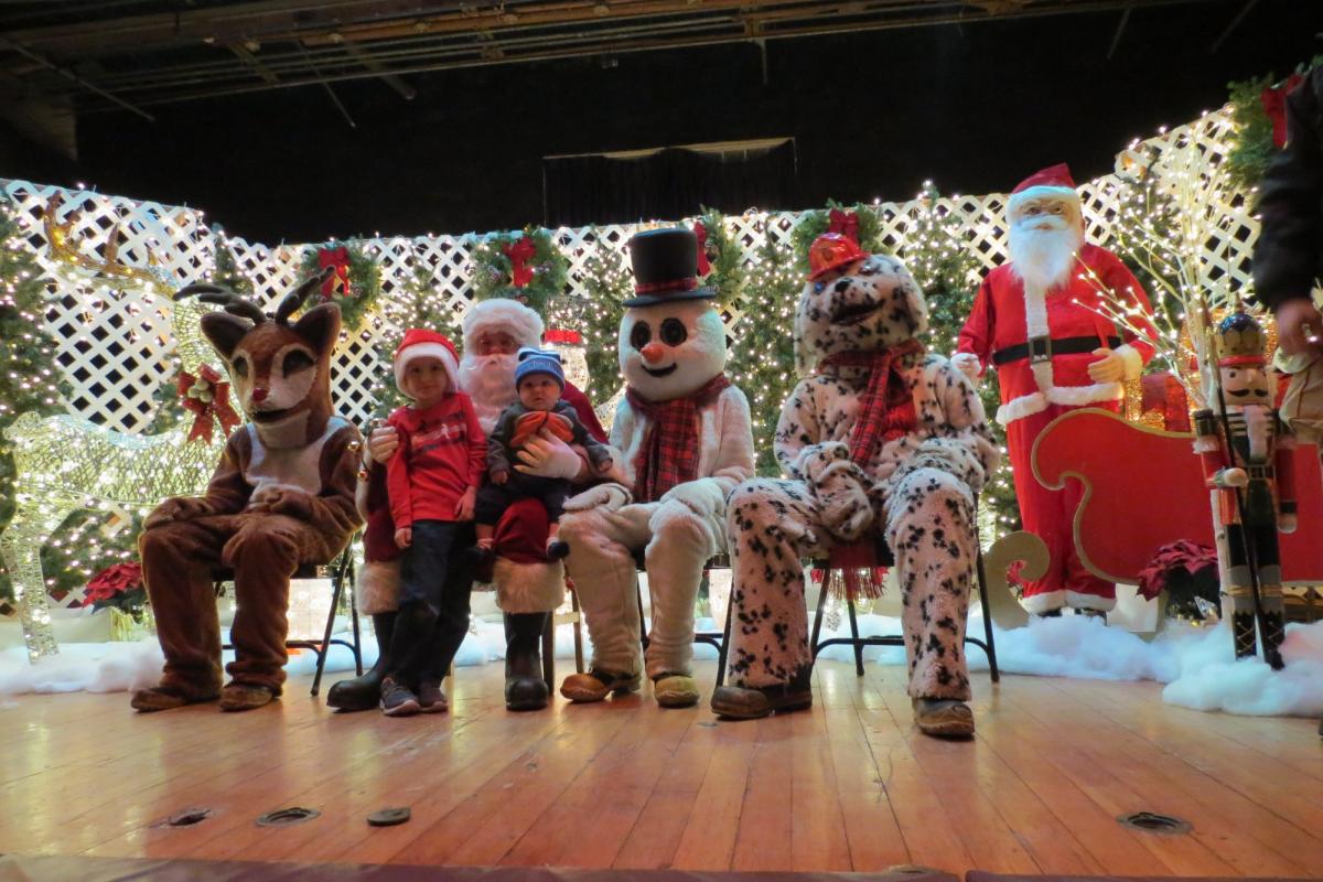 Santa, snowman and reindeer posing with children on stage decorated with Christmas decorations