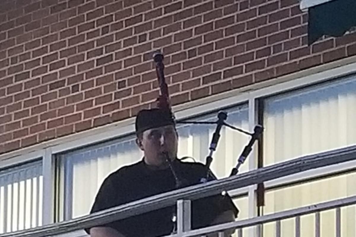 Man in kilt playing bagpipes with building behind him