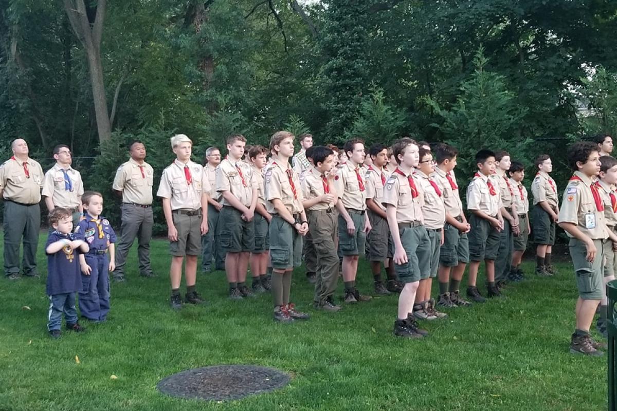 About 25 boy scouts standing in four rows in grass, troop leaders standing in back