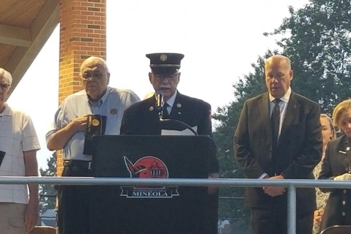 Uniformed man at podium saying prayer, veterans on left standing, four people on right standing