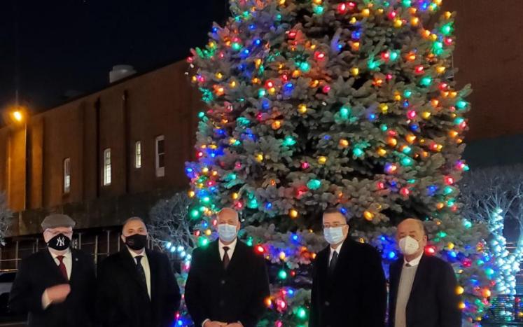 Nighttime, lit Christmas tree with five men in suits wearing masks in front of tree
